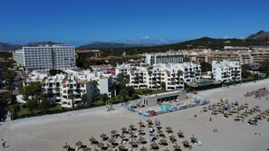 Un complexe hôtelier situé sur la côte, composé de plusieurs bâtiments, dont un grand hôtel doté de balcons et d’un espace piscine.