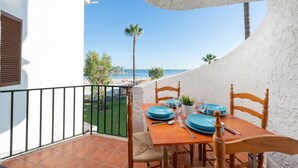 Een eettafel gedekt met blauwe borden en bestek op een balkon met uitzicht op een strand.
