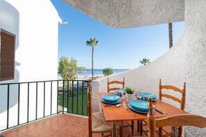 A dining table set with blue plates and silverware on a balcony overlooking a beach. - LORTAL apartment on the first line of the beach with swimming pools (Alcúdia)