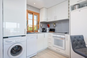 A compact kitchen with a washing machine, oven, and a dining area with a chair.
