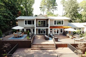 Une maison à deux étages dotée d’une terrasse en bois, d’un espace salon extérieur et d’un patio couvert.