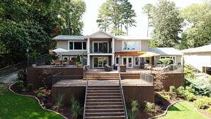 Ein zweistöckiges Haus mit einer Terrasse, Sitzgelegenheiten im Freien und einer Treppe zum Eingang.
