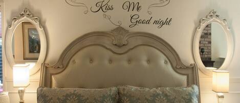 Un dormitorio con cabecera capitonada, dos lámparas de noche y un letrero decorativo en la pared.
