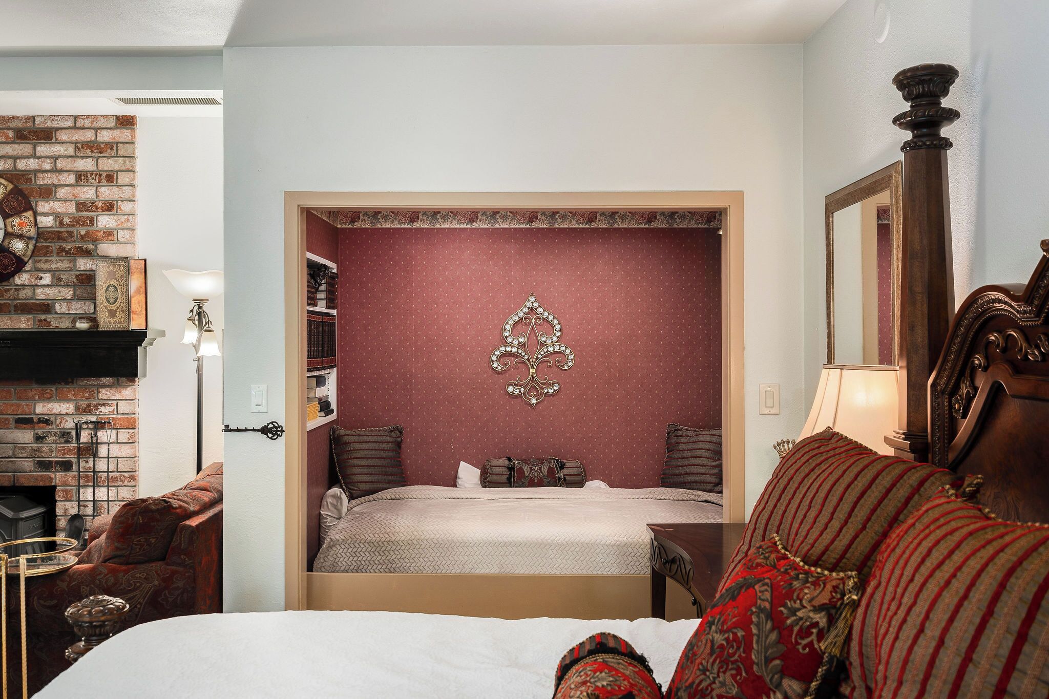 A bedroom with a brick fireplace, a decorative wall piece, a bed with patterned pillows, and a wooden headboard.