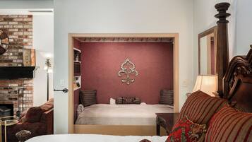 A bedroom with a brick fireplace, a decorative wall piece, a bed with patterned pillows, and a wooden headboard.