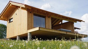 A wooden house with a sloped roof, large windows, and a balcony. - Ferienwohnung Schmalzgrub (Böbrach)