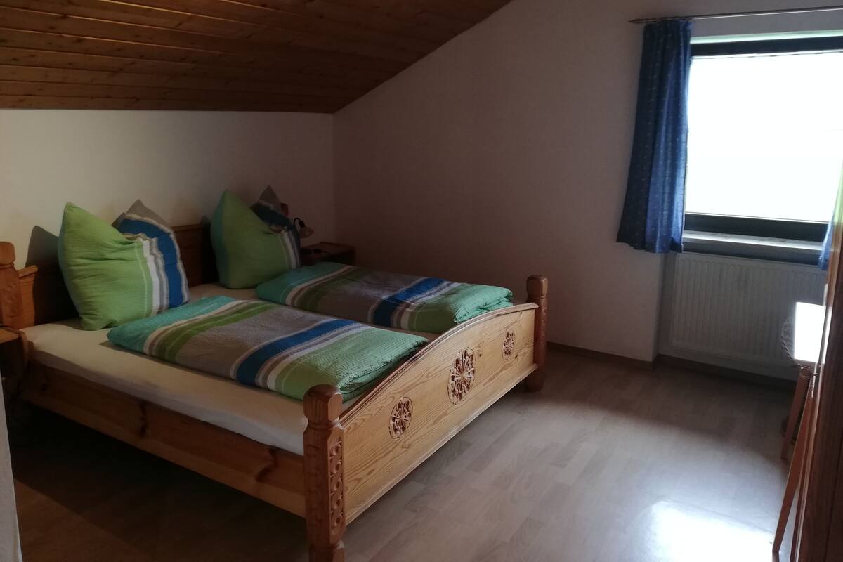 A bedroom with a wooden ceiling, a bed with striped bedding, and a window with blue curtains.