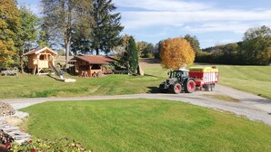 A rural landscape with a wooden playhouse, a tractor with a trailer, and a well-maintained lawn. - Ferienwohnung Schmalzgrub (Böbrach)