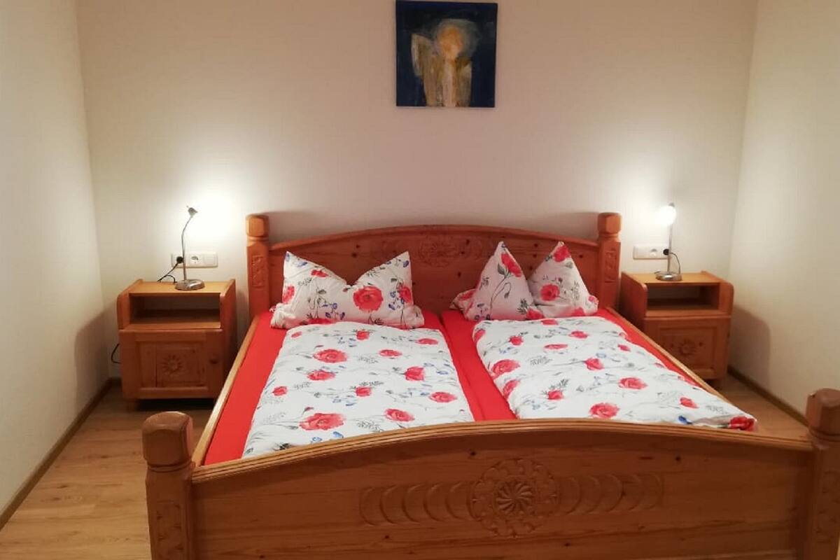 A double bed with floral bedding, wooden headboard, two bedside tables with lamps, and a wall-mounted light fixture.