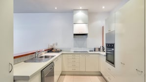 A modern kitchen with white cabinets, a stainless steel sink, a dishwasher, and an oven. - Spacious 2BR Near Westfield Newmarket (Auckland)
