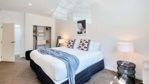 A bedroom with a bed, a bedside table, a lamp, a wardrobe, and a ceiling light. - Spacious 2BR Near Westfield Newmarket (Auckland)