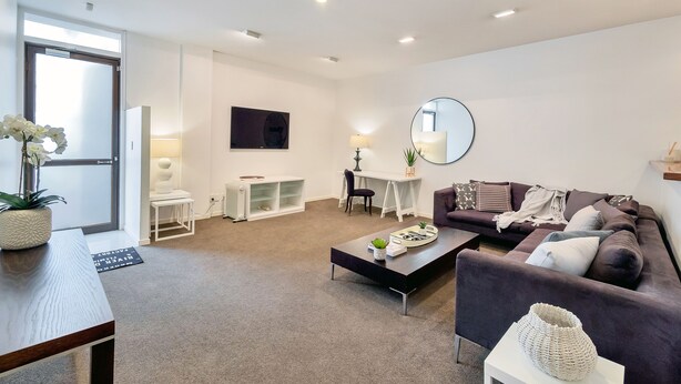 A modern living room with a sofa, coffee table, and a dining area with a table and chairs. - Spacious 2BR Near Westfield Newmarket (Auckland)