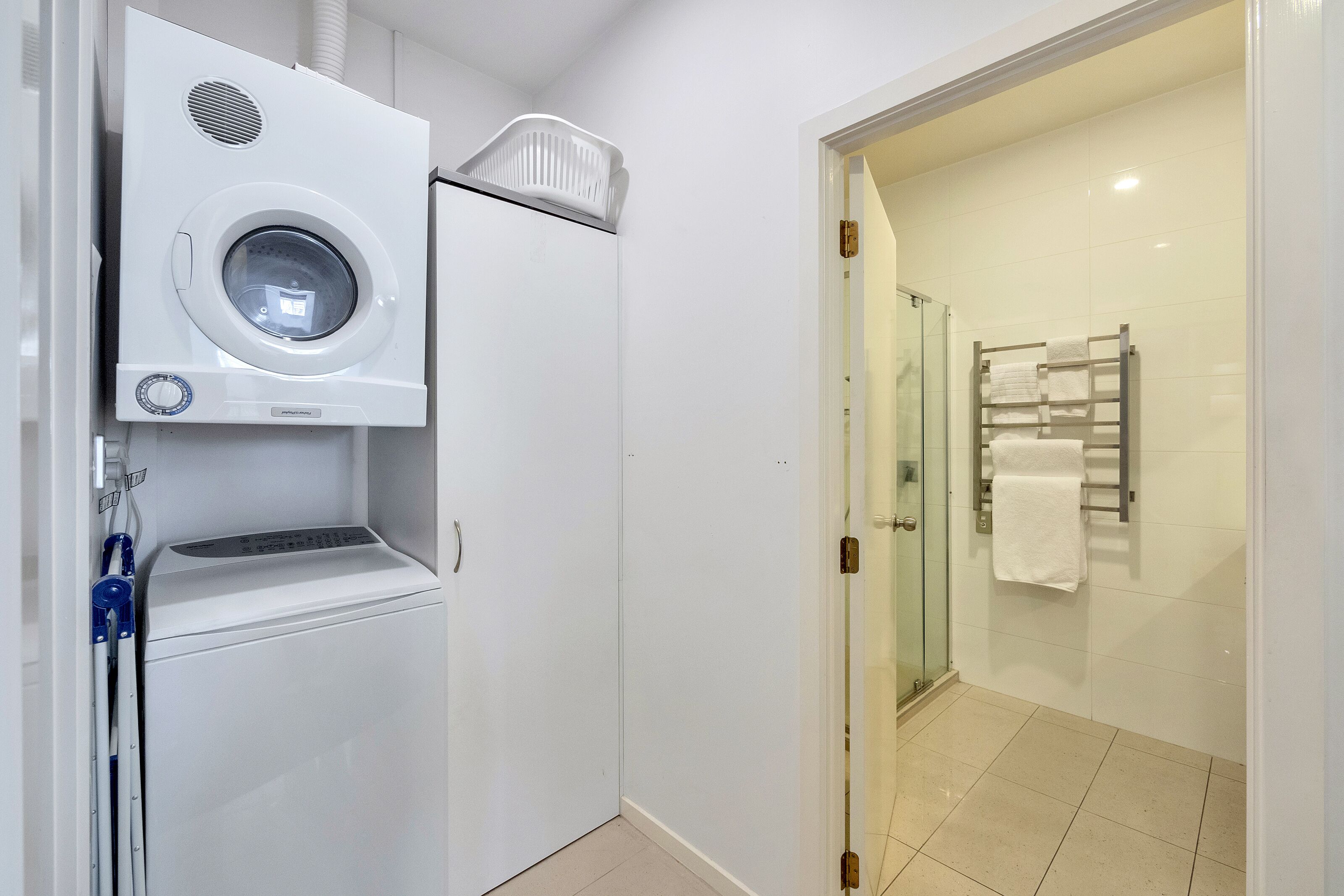 A compact laundry area with a front-loading washing machine and dryer, a glass shower enclosure, and a towel rack.