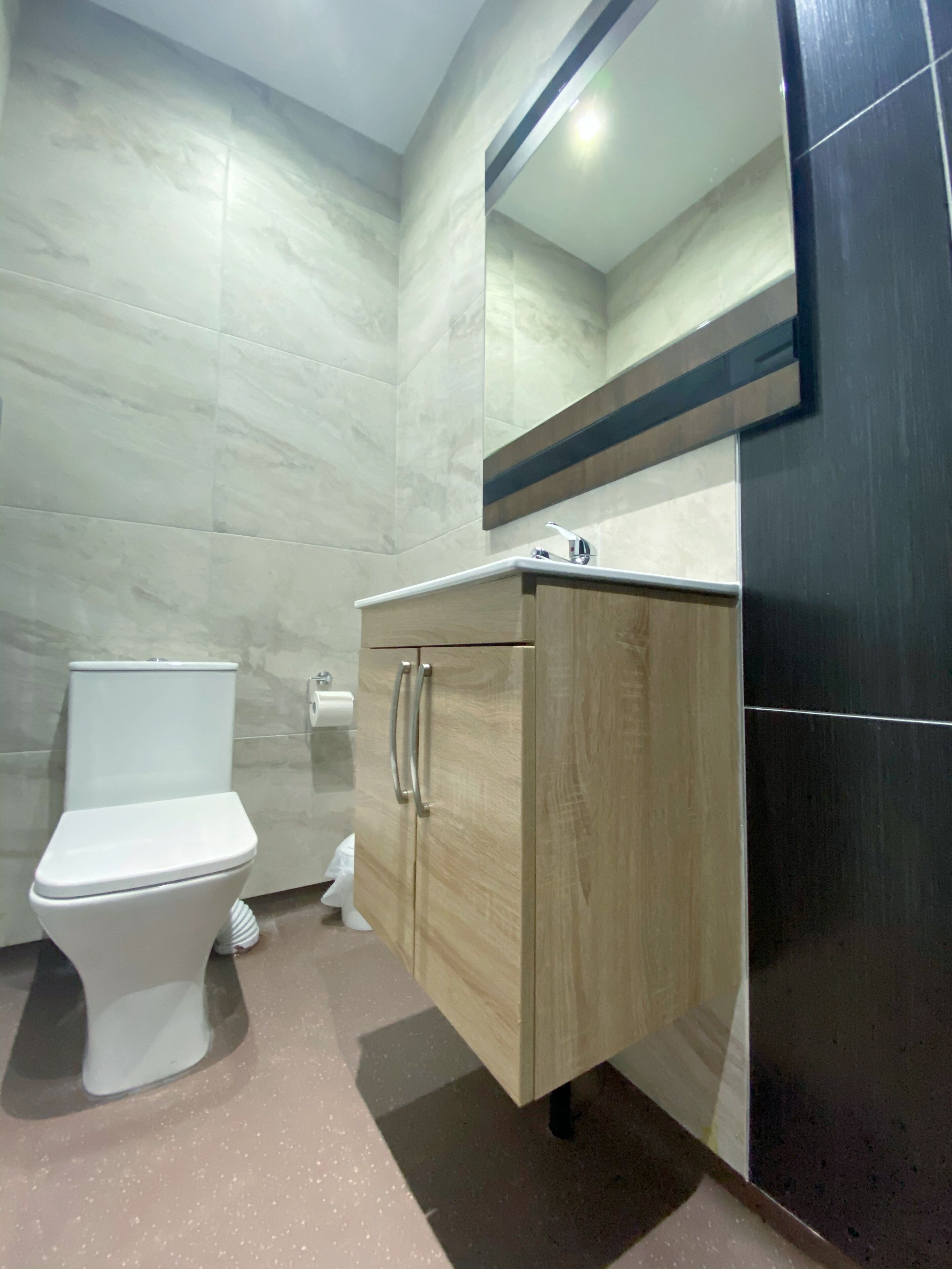 A modern bathroom with a toilet, wooden vanity, and a mirror.