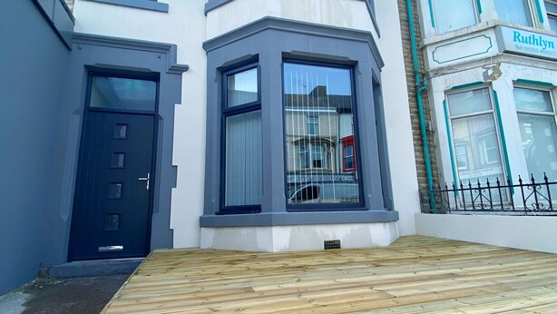 A two-story house with a bay window, a front door, and a wooden deck. - Chelsea Suite Sasco Apartments (Blackpool)