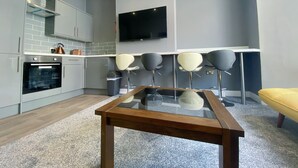 A modern kitchen with grey cabinets, a built-in oven, and a flat-screen TV mounted on the wall. - Chelsea Suite Sasco Apartments (Blackpool)
