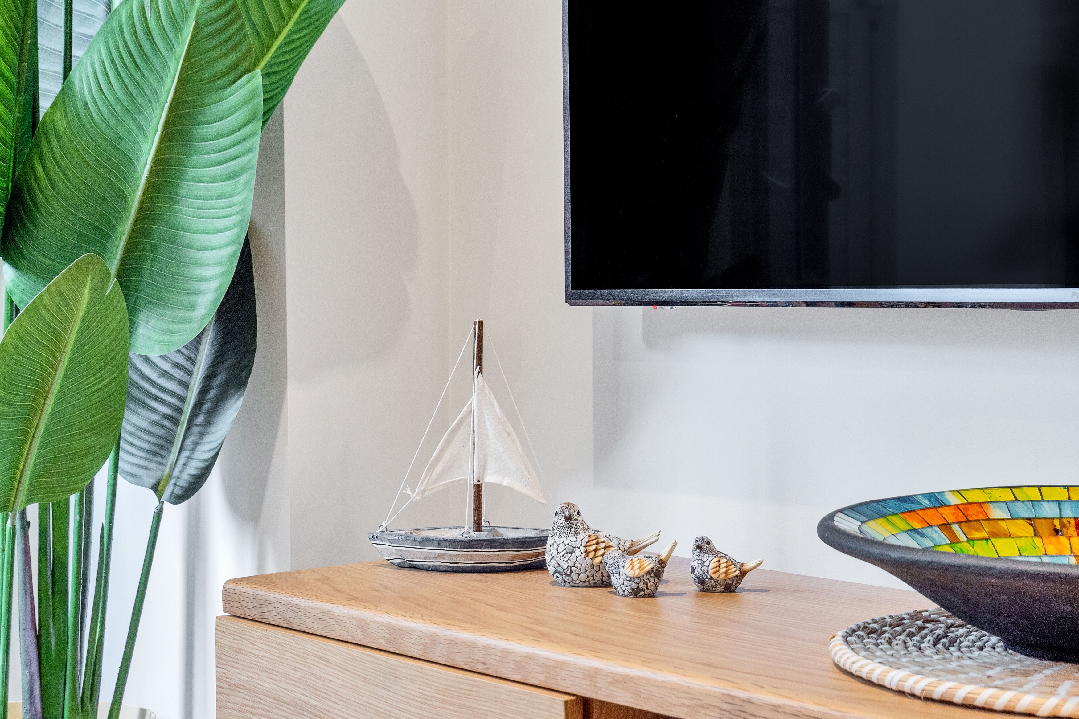 A wooden table with a sailboat model, bird figurines, and a colorful bowl.
