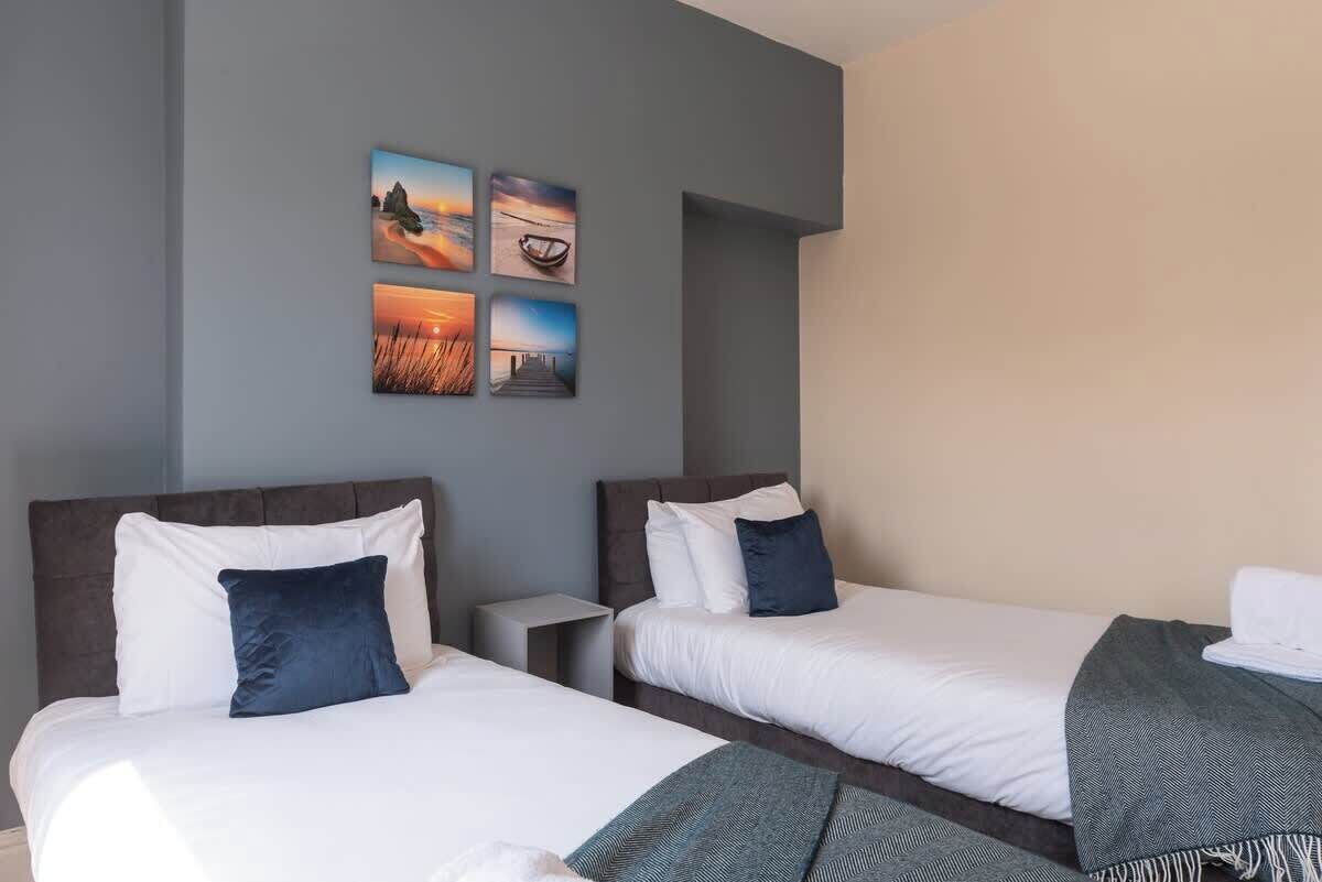 A hotel room with two beds, a nightstand, and a wall with four framed pictures.