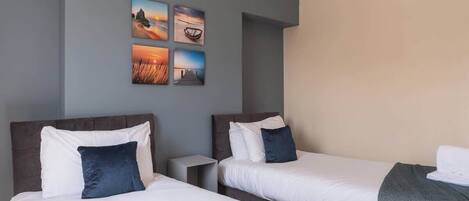A hotel room with two beds, a nightstand, and a wall with four framed pictures.