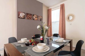 A dining area with a table set for two, a vase with flowers, and a wall with coffee-themed artwork.