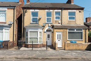 A two-story residential building with a front door, satellite dish, and a small fenced garden area.