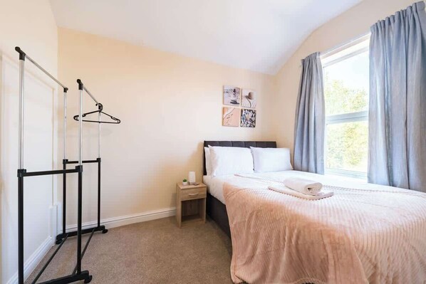A hotel room with a bed, a nightstand, a window with curtains, and a wall-mounted coat rack.
