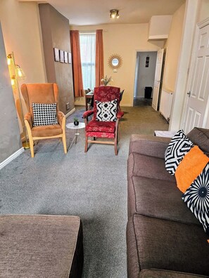 Ein Wohnzimmer mit einem braunen Sofa, einem roten Sessel und einem Holzstuhl mit gemusterten Kissen.