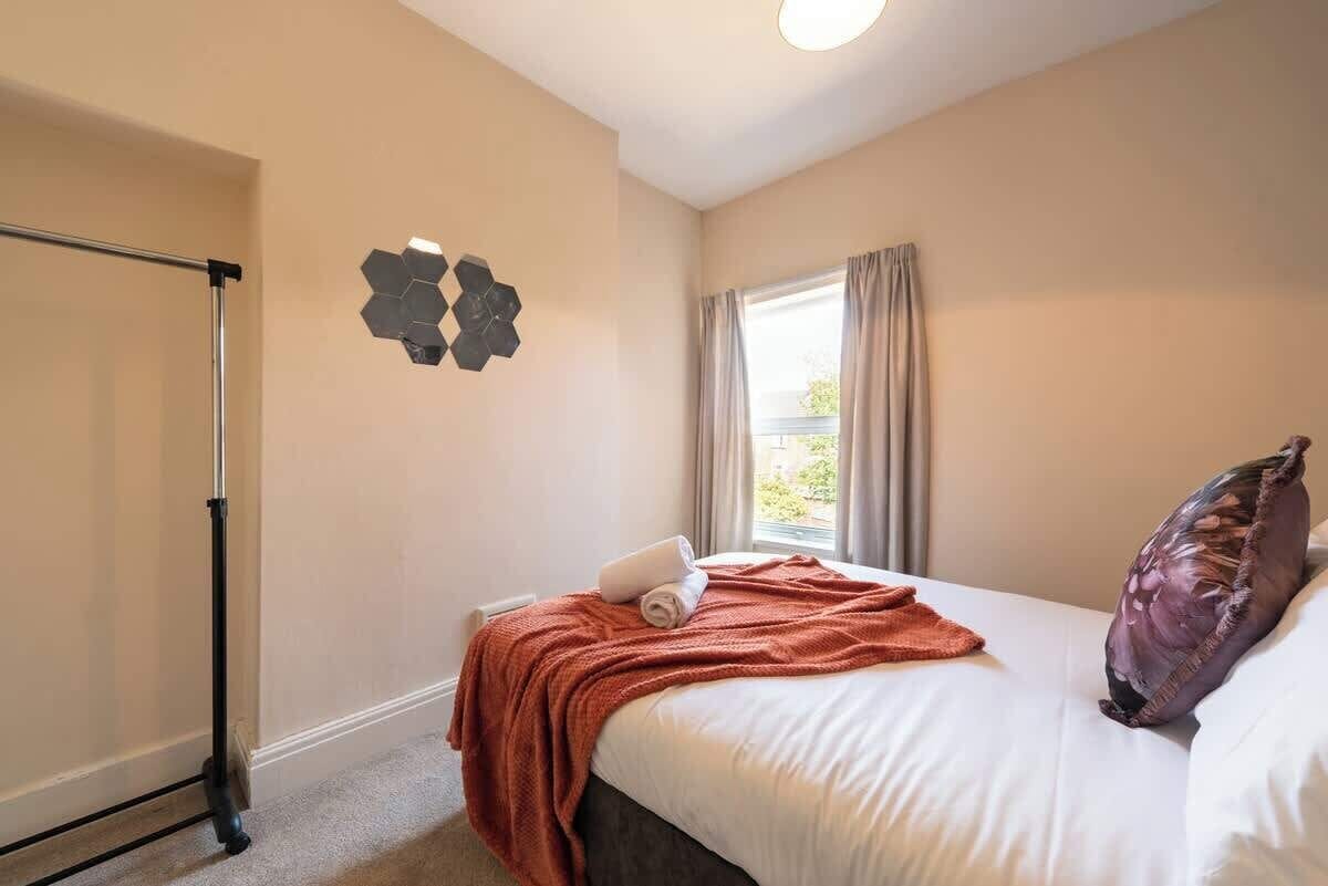 A hotel room with a bed, a window with curtains, a wall-mounted artwork, and a ceiling light.