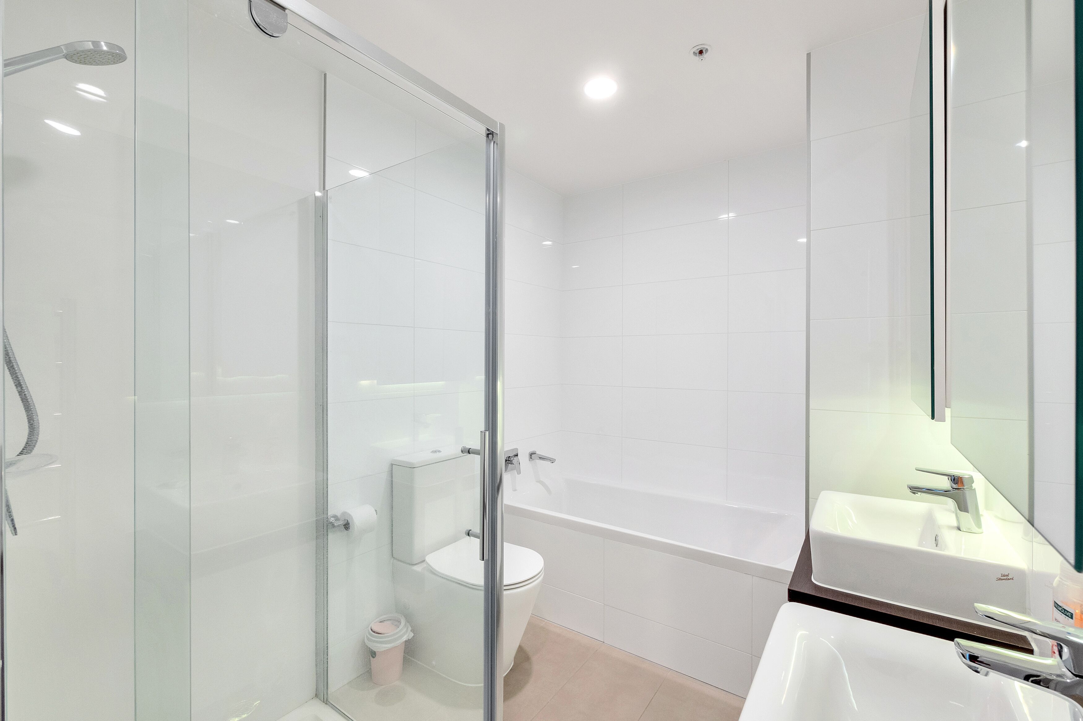 A modern bathroom with a glass shower enclosure, a white toilet, a bathtub, and a sink with a mirror.