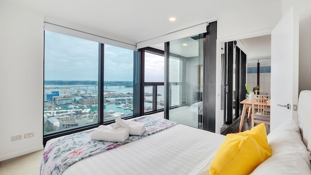 Habitación de hotel moderna con una cama grande, vista a la ciudad y un balcón con zona de comedor.