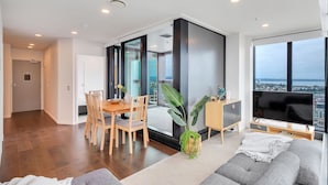 Una sala de estar moderna con un sofá, una zona de comedor con una mesa y sillas, un televisor y un ventanal con vistas a la ciudad.