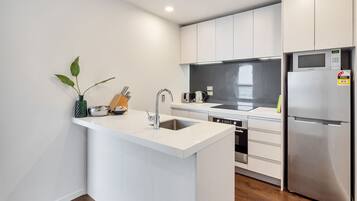 A modern kitchen with white cabinetry, stainless steel appliances, a built-in island with a sink, and a small plant.