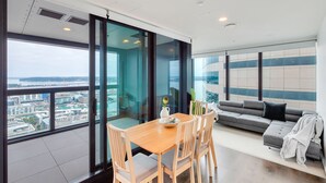 Una sala de estar moderna con una mesa de comedor y sillas, un sofá gris y un ventanal con vistas a la ciudad.