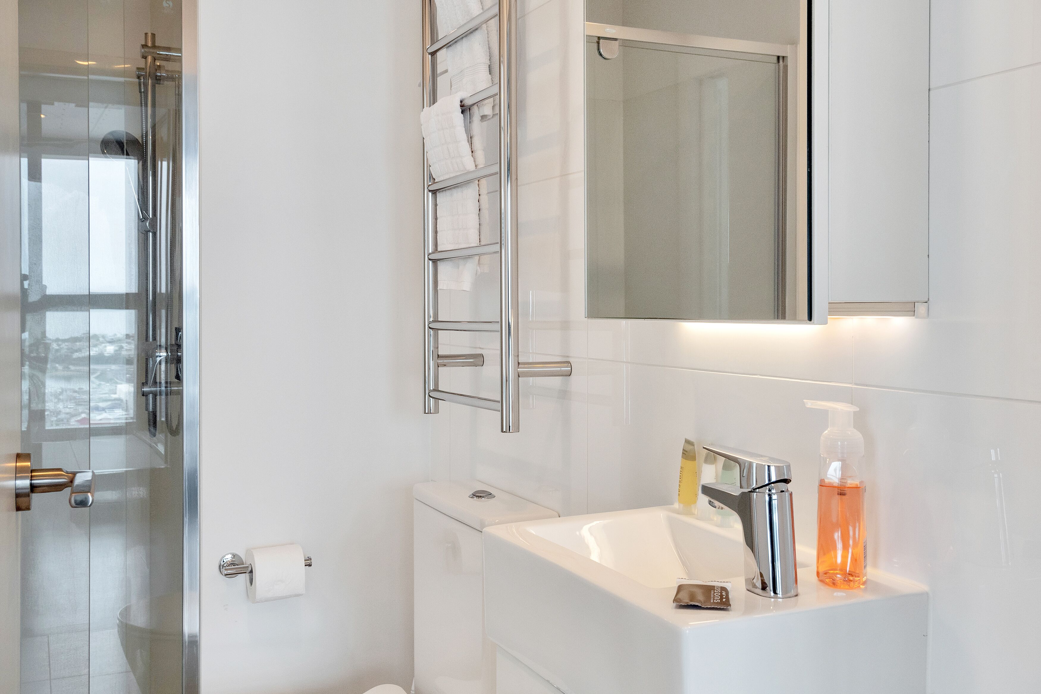 A modern bathroom with a glass shower enclosure, a white sink with a chrome faucet, and a mirror above the sink.