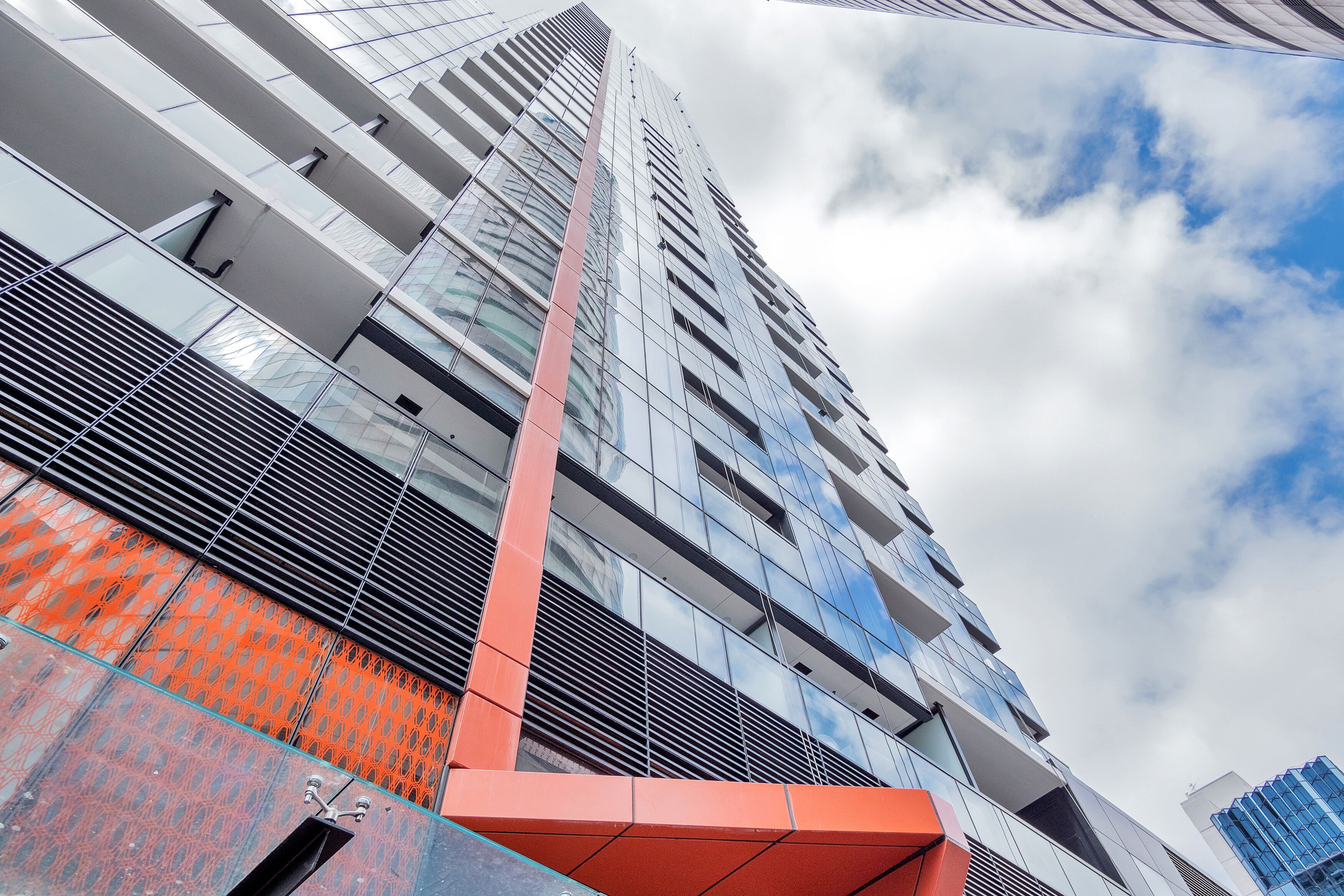 Un immeuble moderne de grande hauteur, doté de fenêtres en verre réfléchissant et d’un élément structurel rouge bien visible.