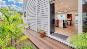 A modern house with a wooden deck, a sliding glass door leading to a kitchen and living area, and potted plants on the deck. - Elegant and Stylish Retreat in Epsom (Auckland)