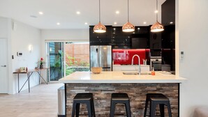 A modern kitchen with a large island, black bar stools, and pendant lighting. - Elegant and Stylish Retreat in Epsom (Auckland)