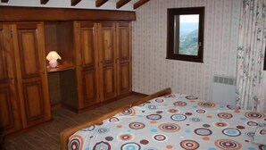 A bedroom with a bed, wooden wardrobe, and a window with a view.