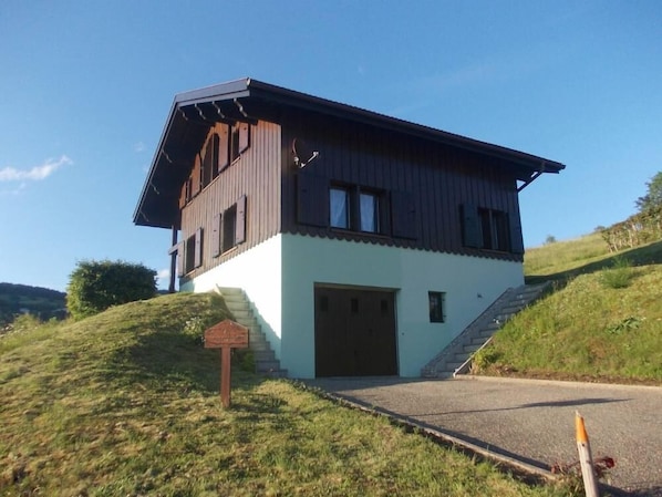 Ein zweistöckiges Haus mit Garage, gelegen auf einem grasbewachsenen Hügel.