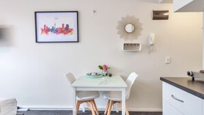 Una cucina moderna con un tavolo bianco, due sedie, un quadro con vista sulla città, uno specchio decorativo e un forno a incasso.