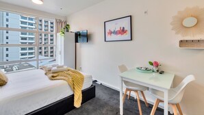 Una camera d'albergo con un letto, una scrivania, una sedia, una TV e vista sulla città.
