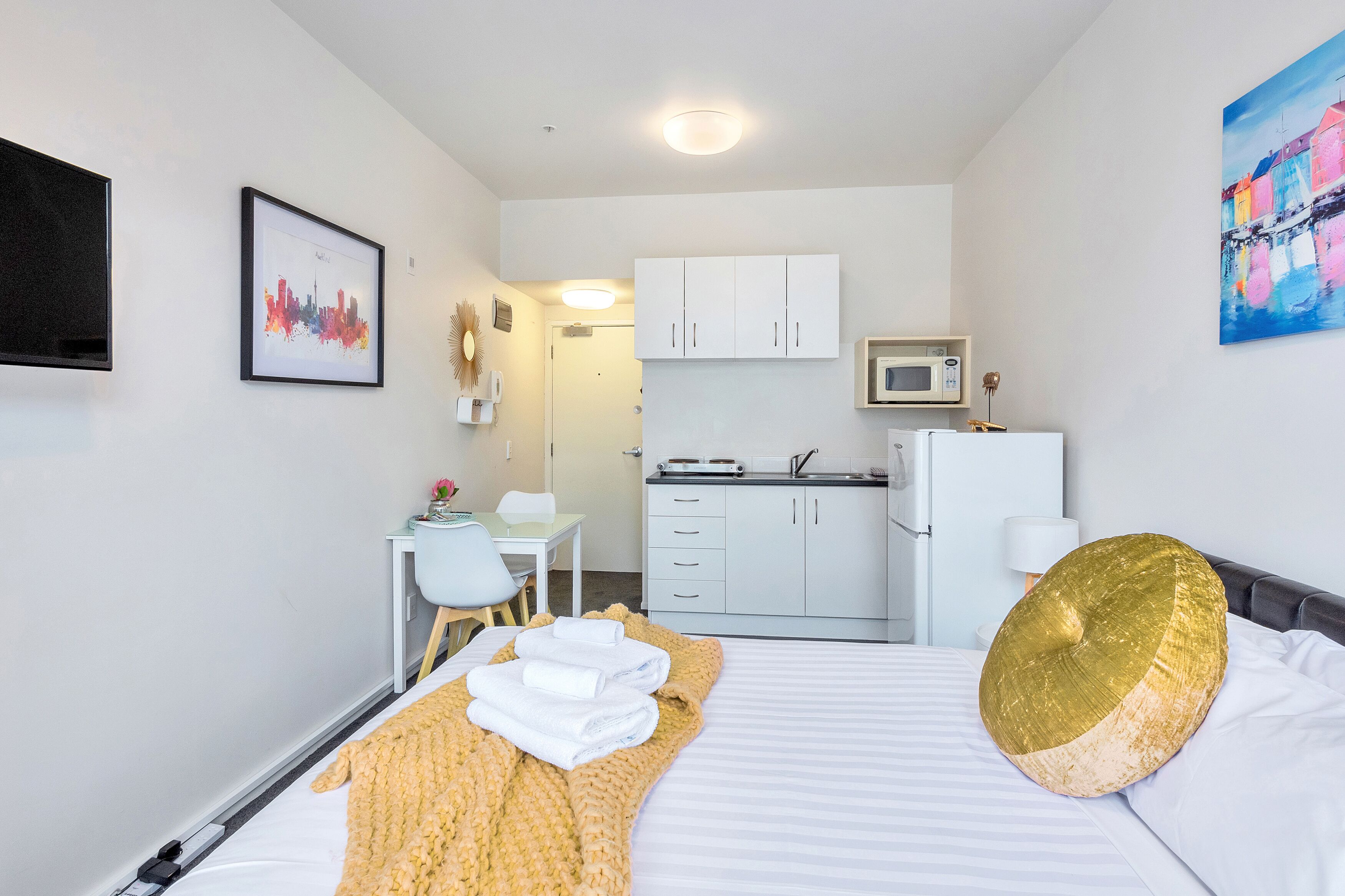 A compact hotel room with a bed, a desk, a kitchenette, and a bathroom.