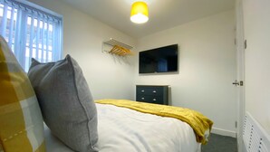A bedroom with a bed, a television, a heater, and a window with blinds. - Kensington Suite Sasco Apartments (Blackpool)