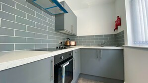 A compact kitchen with grey cabinets, a built-in oven, a kettle, and a toaster. - Kensington Suite Sasco Apartments (Blackpool)