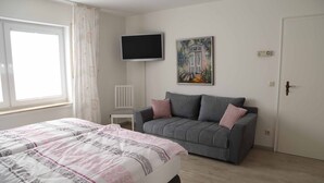 Un dormitorio con una cama, un sofá gris, un televisor y un cuadro en la pared.