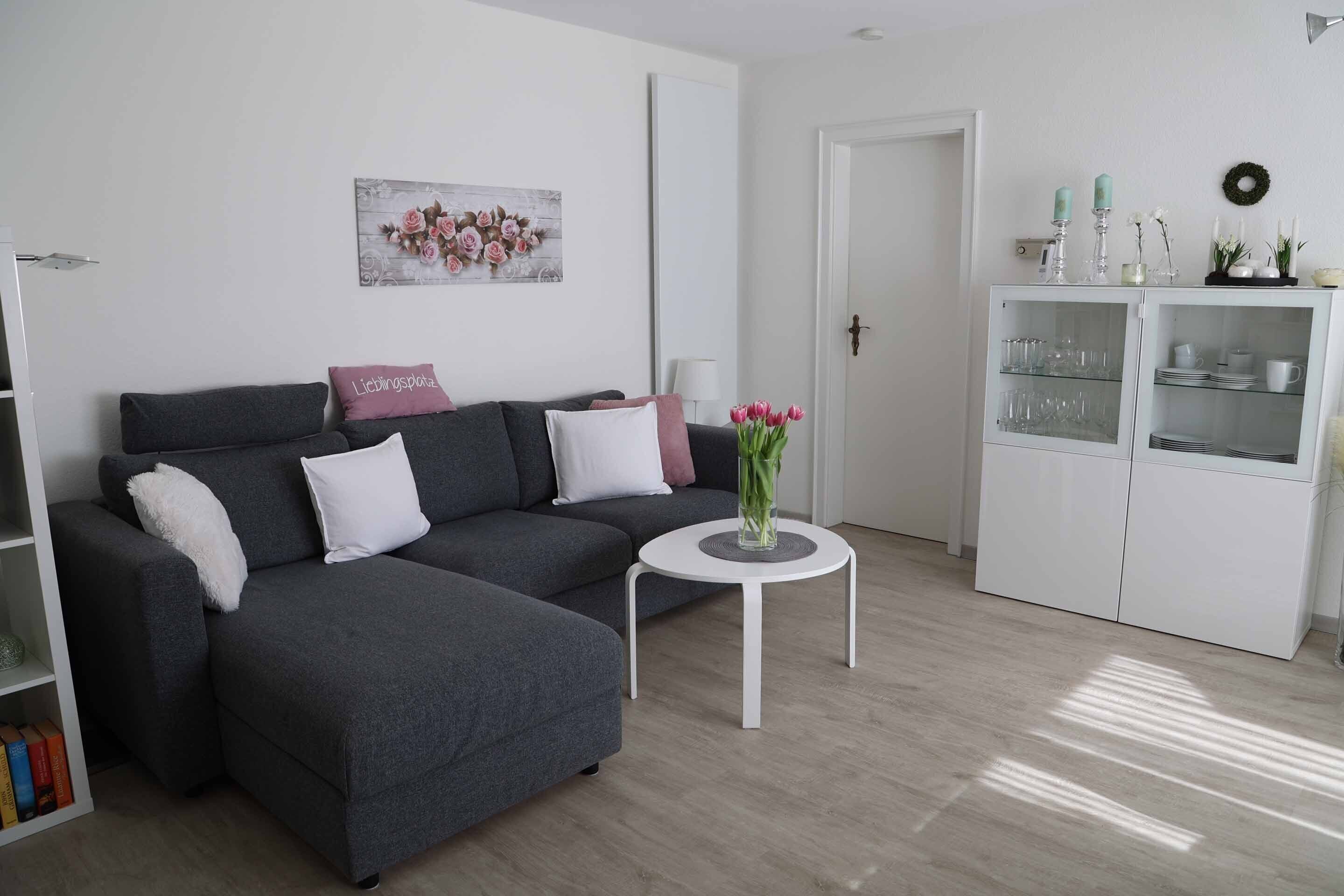 Ein modernes Wohnzimmer mit einem grauen Ecksofa, einem weißen Couchtisch und einer weißen Vitrine mit Glastüren.