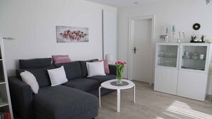 Una sala de estar moderna con un sofá seccional gris, una mesa de centro blanca y un mueble blanco con puertas de vidrio.
