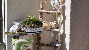 Un espacio de estar rústico al aire libre con un tocón de abedul, una cesta tejida con flores y una escalera de madera con un letrero que dice 'Welcome'.
