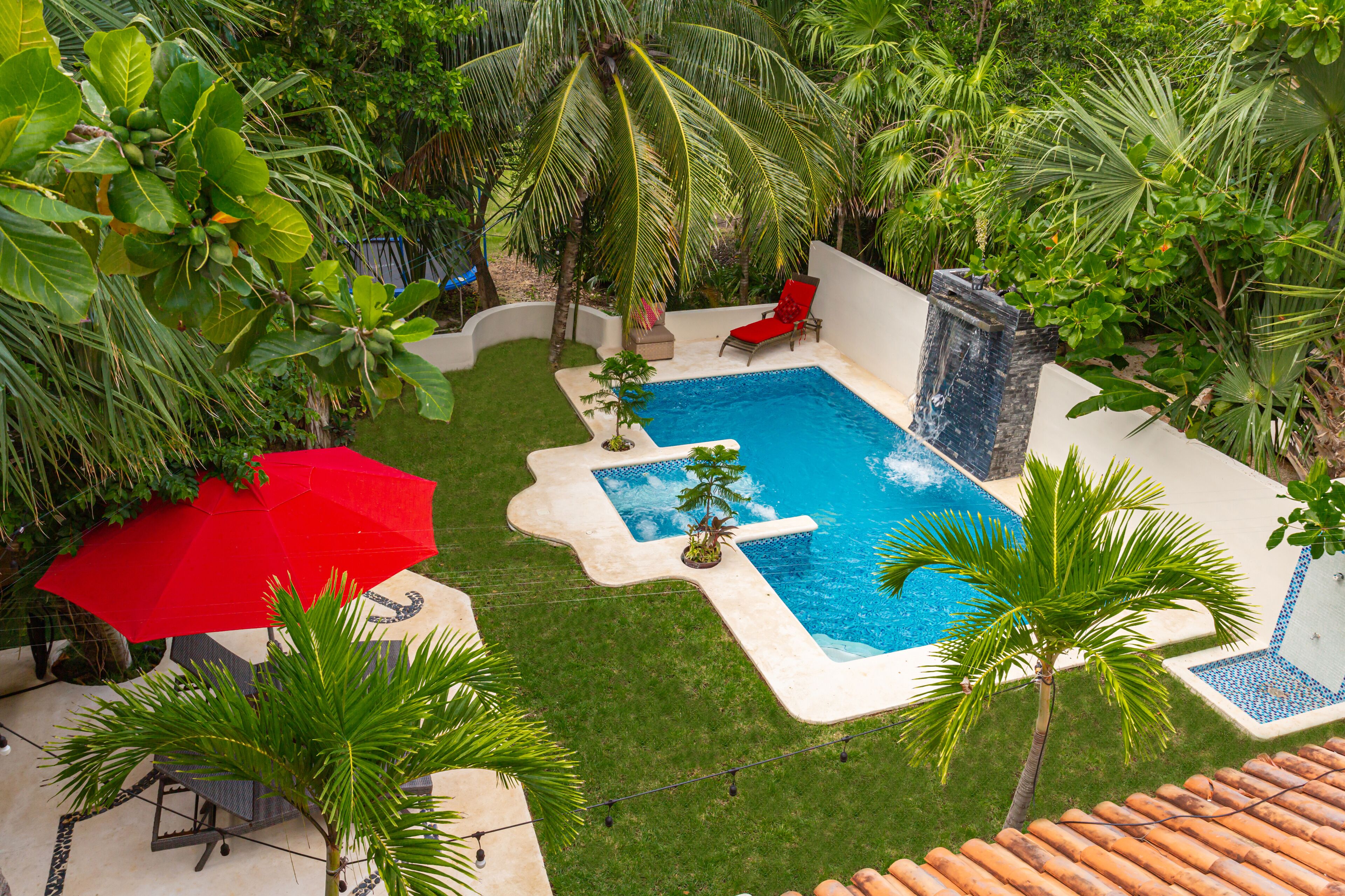 A backyard with a swimming pool, a red umbrella, and a red lounge chair.