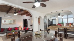A spacious living room with a glass-top dining table, comfortable seating, and a kitchen area with modern appliances. - Villa Corazon Deluxe (Puerto Aventuras)